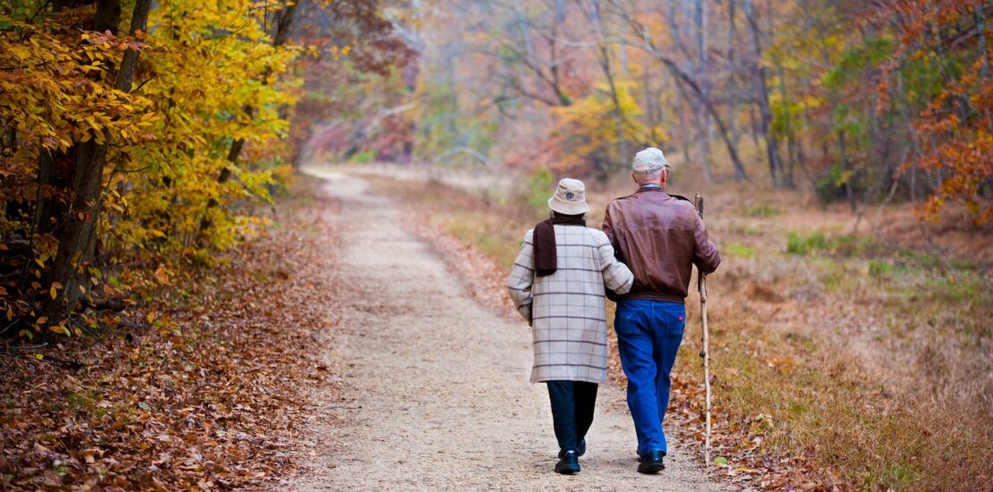 Couple walking confidently through vibrant fall foliage in golden afternoon light